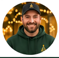 Circular portrait of a smiling man in a black cap and dark green hoodie, with warm holiday lights in the background.