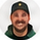 Circular user avatar of a smiling man wearing a dark cap and dark shirt.