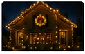 Night house photo with warm holiday lights and a lit wreath focal point.