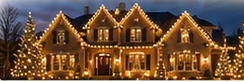 Twilight exterior photograph of a large house lavishly covered in warm white lighting and illuminated trees.
