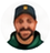 Circular headshot of Alex Johnson, bearded man wearing a dark cap and dark shirt against a warm outdoor background.